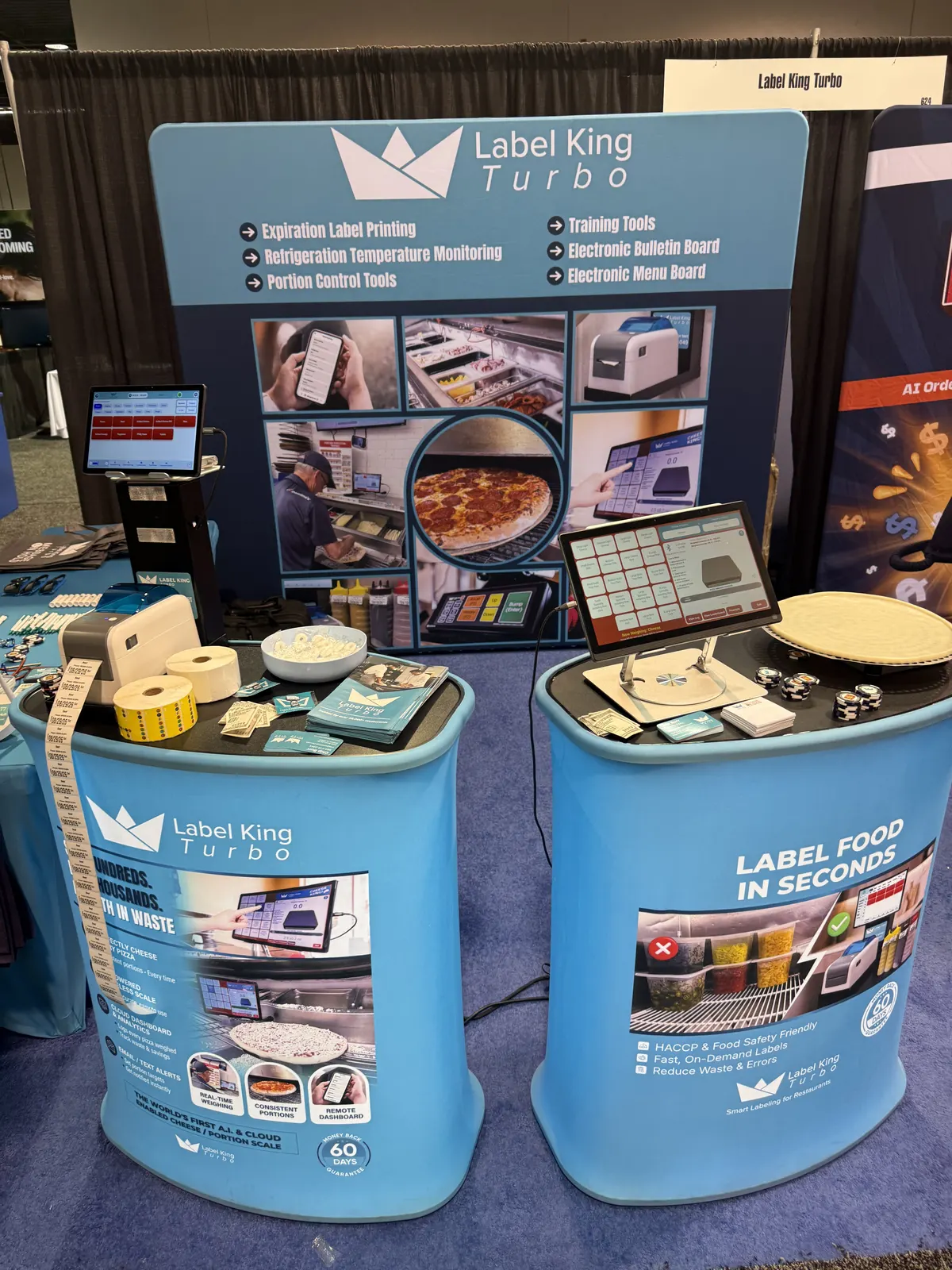 Label King Turbo booth at the California Restaurant Show with branded demo counters, a label printer, label rolls, and tablet displays running the labeling app