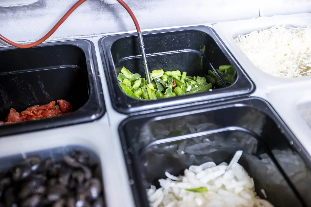 Temperature probe reading chopped vegetables in a chilled prep-line insert